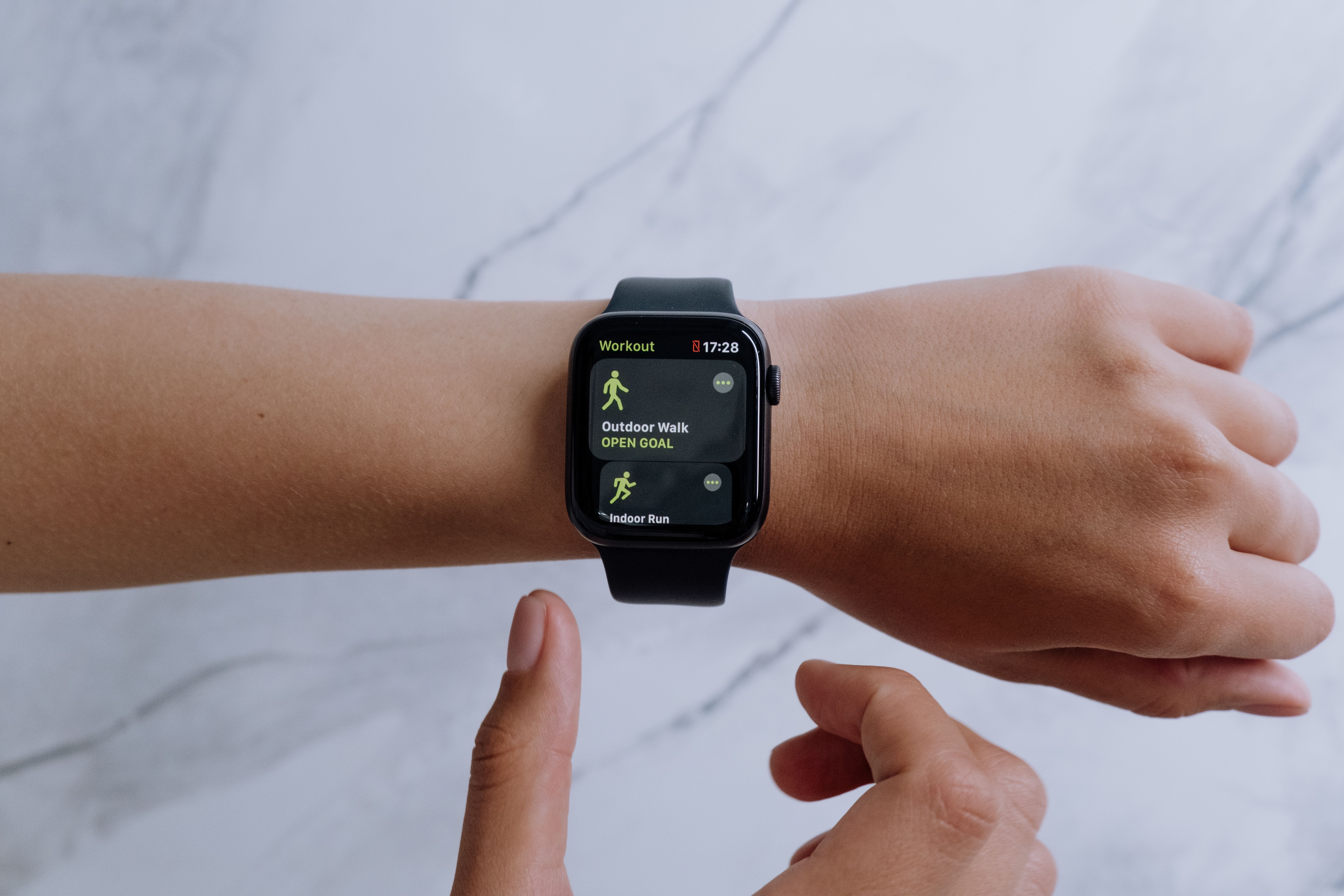 Person wearing a black budget smartwatch showing a fitness tracking app on a marble surface